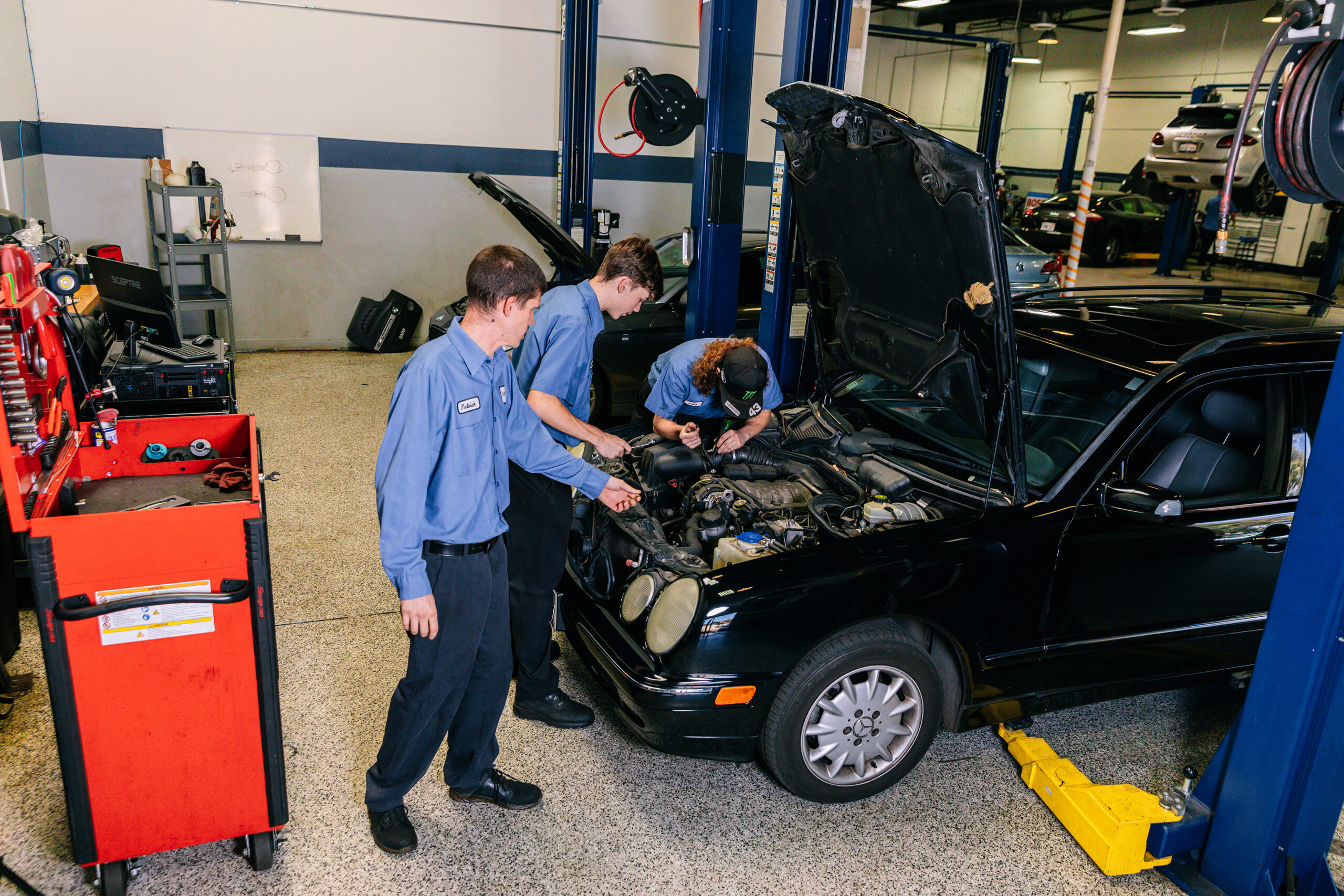 Three Project Workforce students look under the hood of a black car.